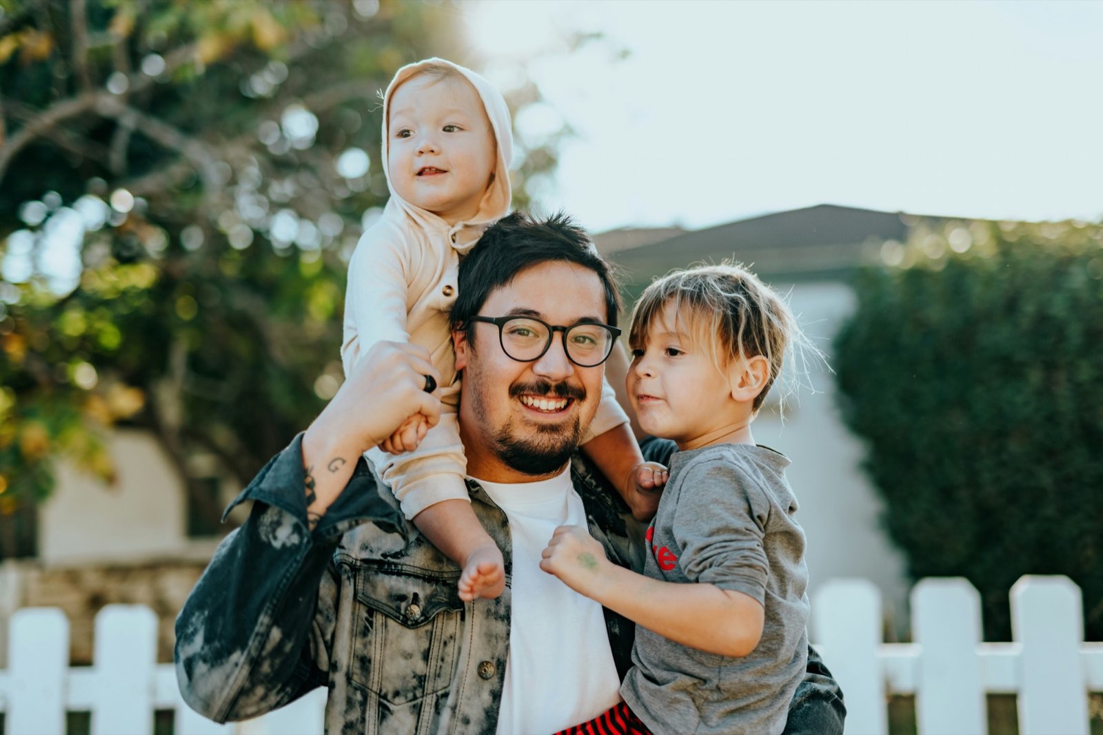 A father and his two young children smiling outside their home